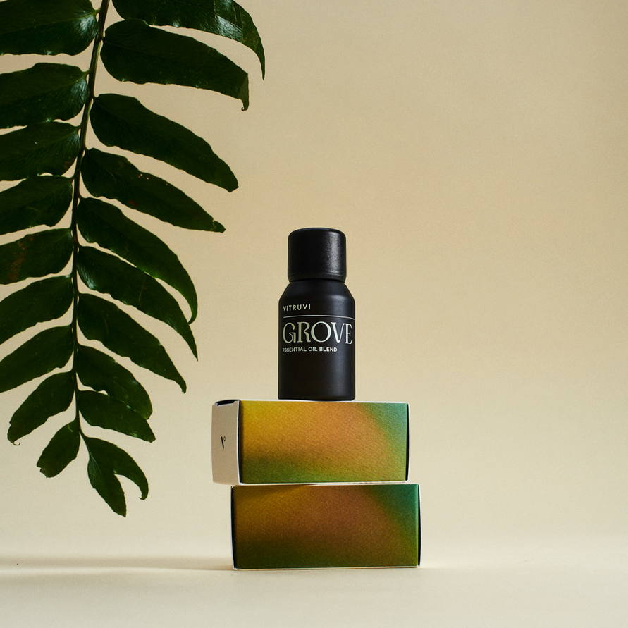 A bottle of essential oil sits atop two boxes. A leaf frames the left hand corner of the image. 