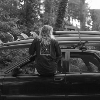 Blonde model sitting out car window wearing Goofy Apparel Dark Brown T with back graphic