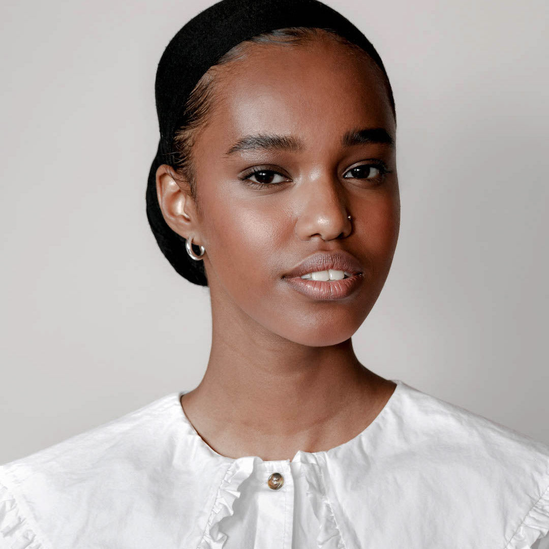 A woman wears the silver hoop earrings. They hug her ears delicately and pop against the white background. 